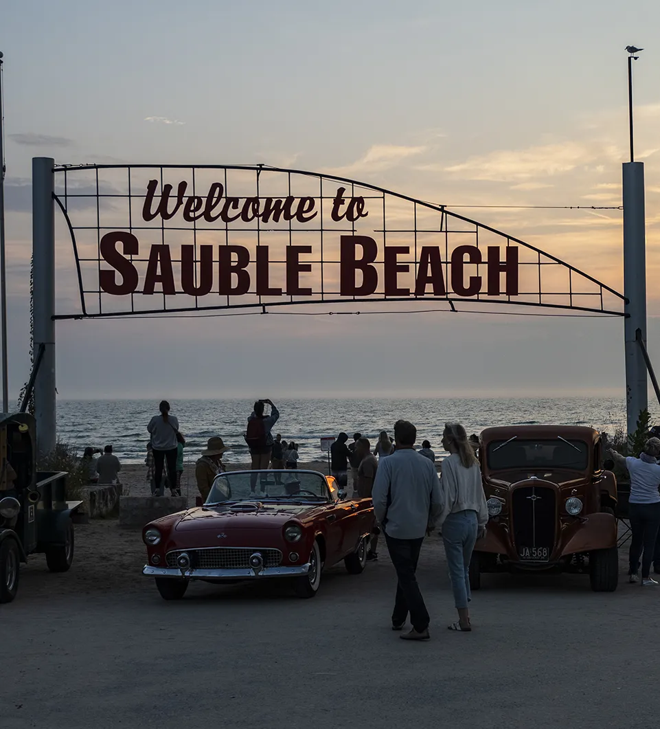 Sauble Beach arch sign with classic cars at base. Taken at sunset